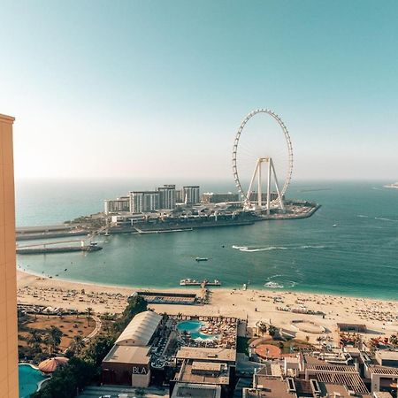 Amwaj Rotana, Jumeirah Beach - Dubai Exterior photo The photo shows a stunning coastal view featuring a large Ferris wheel, likely situated on an island or seaside area. In the foreground, there is a high-rise building with a distinctive logo, while below, you can see a beach with umbrellas and people
