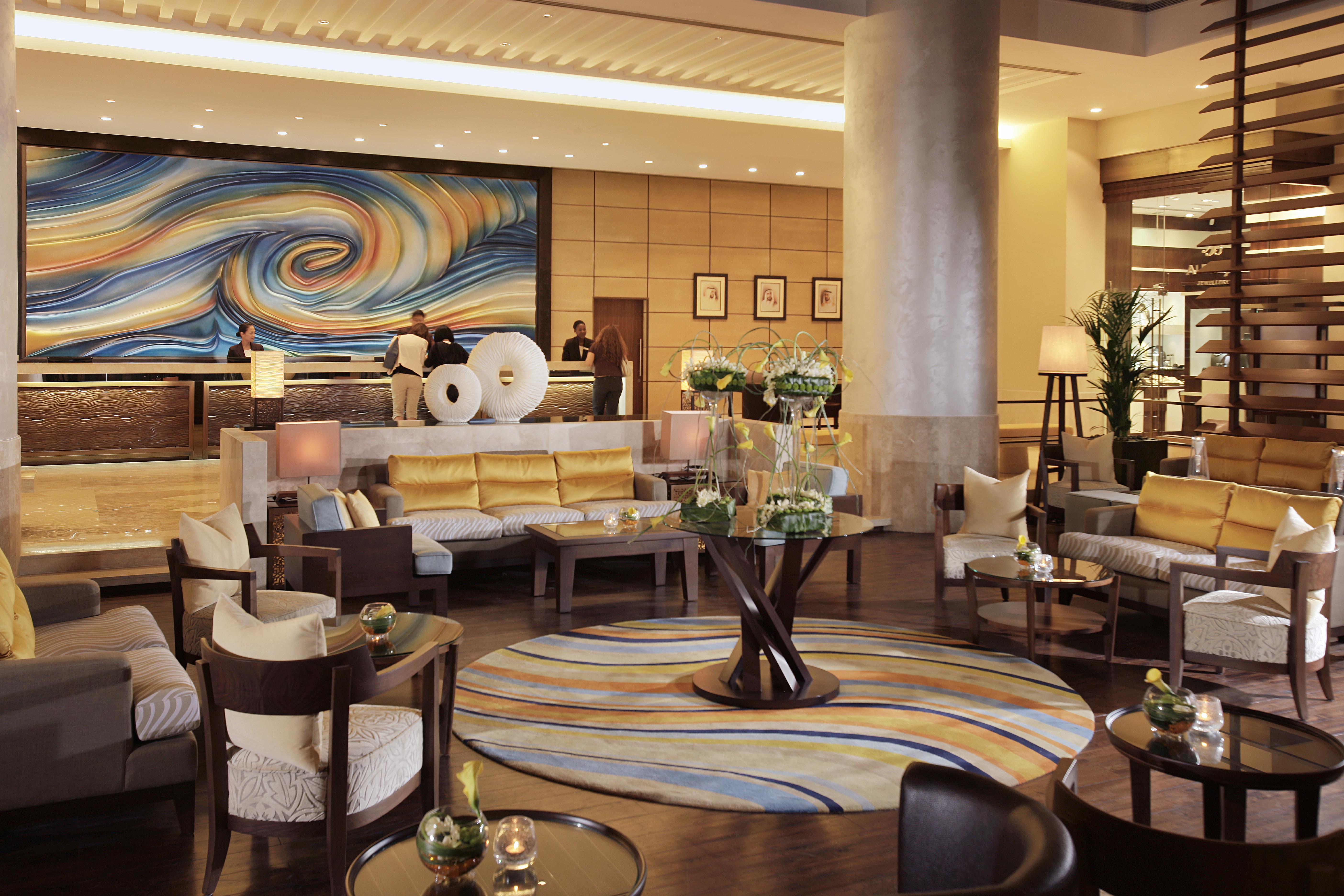 Amwaj Rotana, Jumeirah Beach - Dubai Interior photo The photo shows a stylish and contemporary hotel lobby. It features a spacious seating area with comfortable sofas and armchairs arranged around coffee tables. The decor includes a large, vibrant mural with swirling colors on one wall, adding an arti