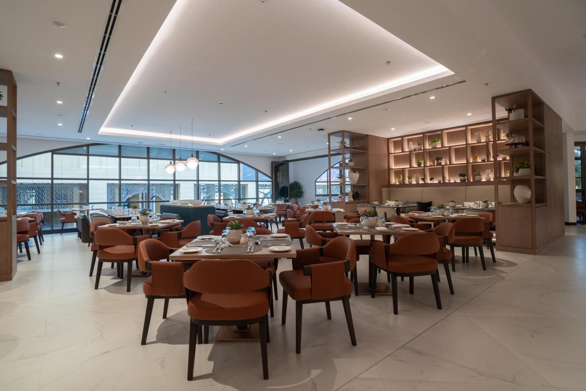 Amwaj Rotana, Jumeirah Beach - Dubai Exterior photo The photo shows a modern restaurant interior. It features a spacious dining area with neatly arranged tables and stylish chairs. The color scheme includes warm tones, with brown chairs and light-colored surfaces. The ceiling has a sleek design with s