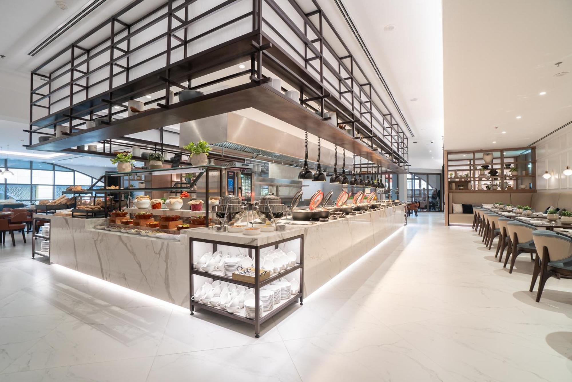 Amwaj Rotana, Jumeirah Beach - Dubai Exterior photo The photo depicts a modern dining area, likely a restaurant or a buffet setup. The interior features a spacious layout with a central serving area made of marble. This area is equipped with various food items displayed in a visually appealing manner.