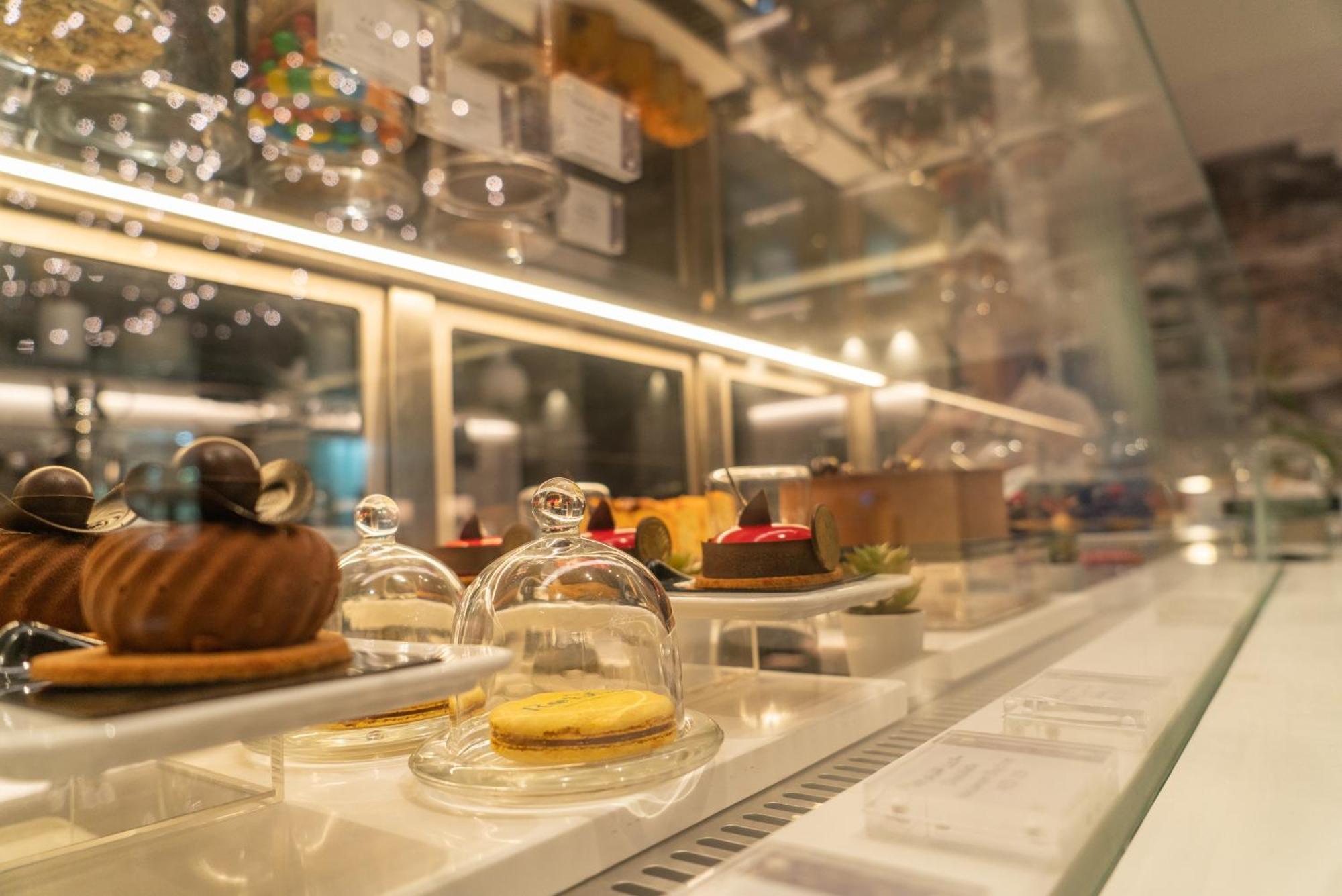 Amwaj Rotana, Jumeirah Beach - Dubai Exterior photo The photo shows a display case featuring a variety of desserts. Each dessert is presented under a small glass dome, showcasing their intricate designs. The treats include a round chocolate pastry, a small cake topped with colorful fruits, and a yello