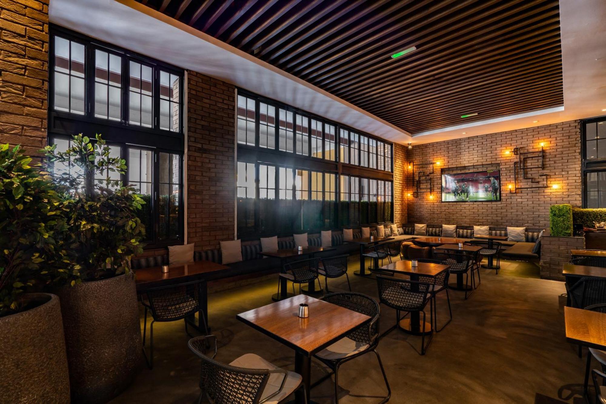 Amwaj Rotana, Jumeirah Beach - Dubai Exterior photo The photo shows a modern interior of a restaurant or café. It features a spacious area with large windows allowing natural light to enter. The walls are a combination of brick and wood, creating a warm atmosphere. There are several tables with chairs
